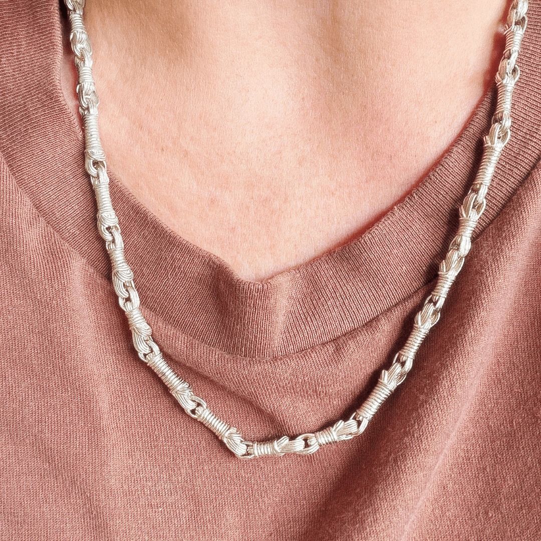Close-up of the Breindell Tzitzit I Necklace №2 in 925 Sterling Silver, worn by a woman over a terracotta-toned shirt. The contemporary architectural pendant features 28 interlocking links. Premium Israeli-designed jewelry that combines minimalist Bauhaus aesthetics with sacred Jewish symbolism.