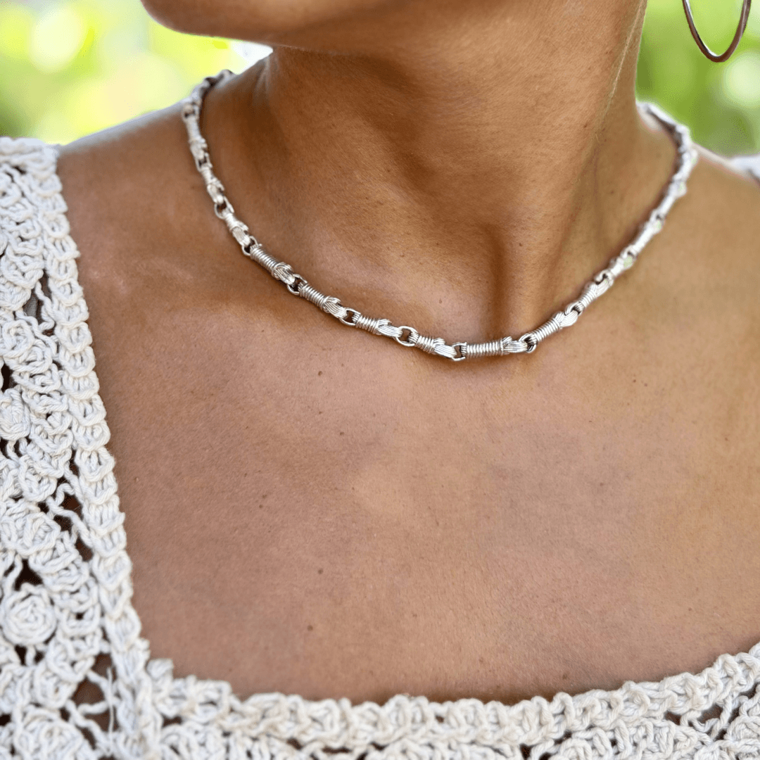 Front view of a female model wearing the Breindell Tzitzit I Necklace №2 in Sterling Silver, styled with a cream crochet top against a background of green trees.