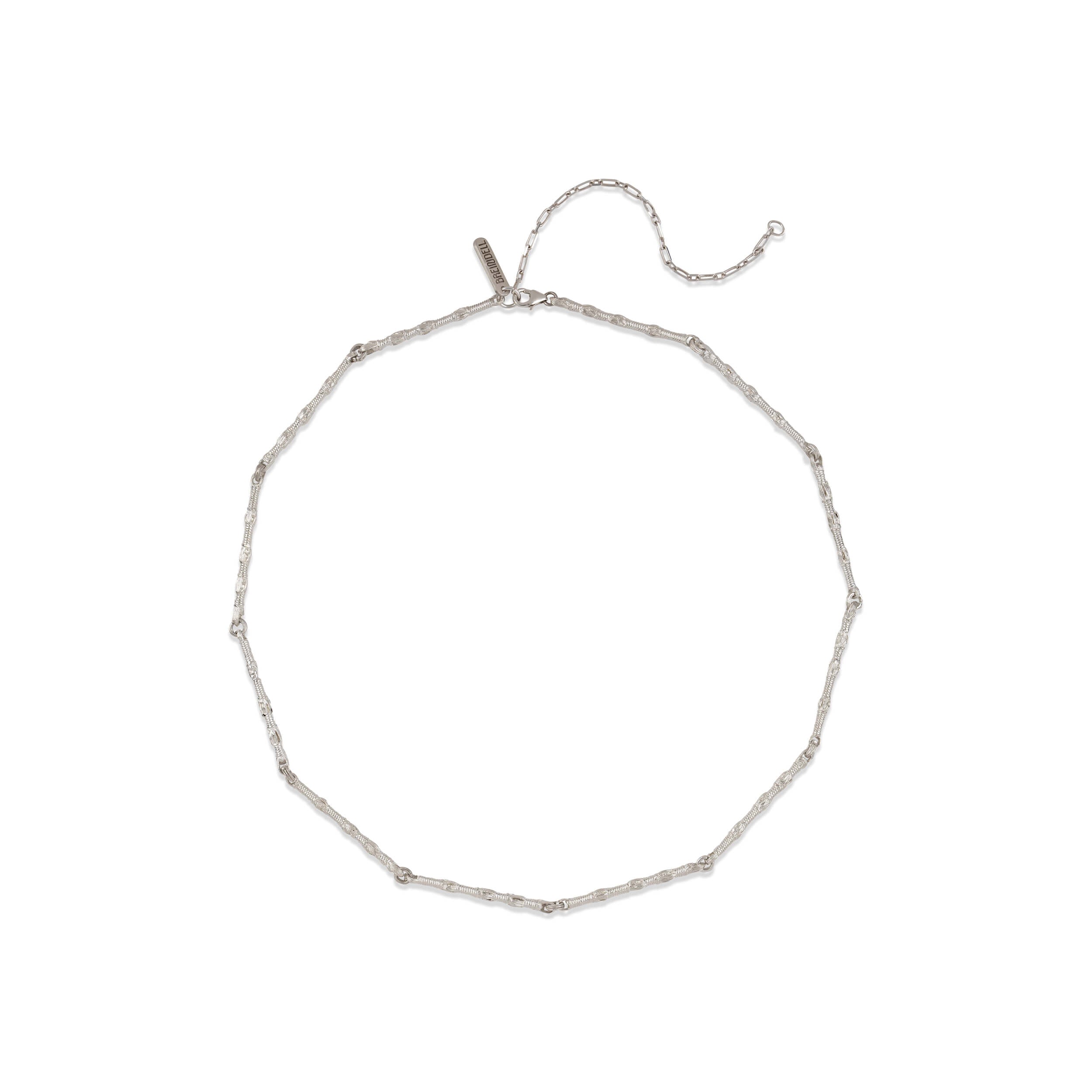 A minimalist flat lay of the Breindell Tzitzit I Necklace №1 in 925 sterling silver. The composition highlights the linear precision and architectural symmetry of the integrated knot and chain, presented with a clean, soft shadow on a stark white background.