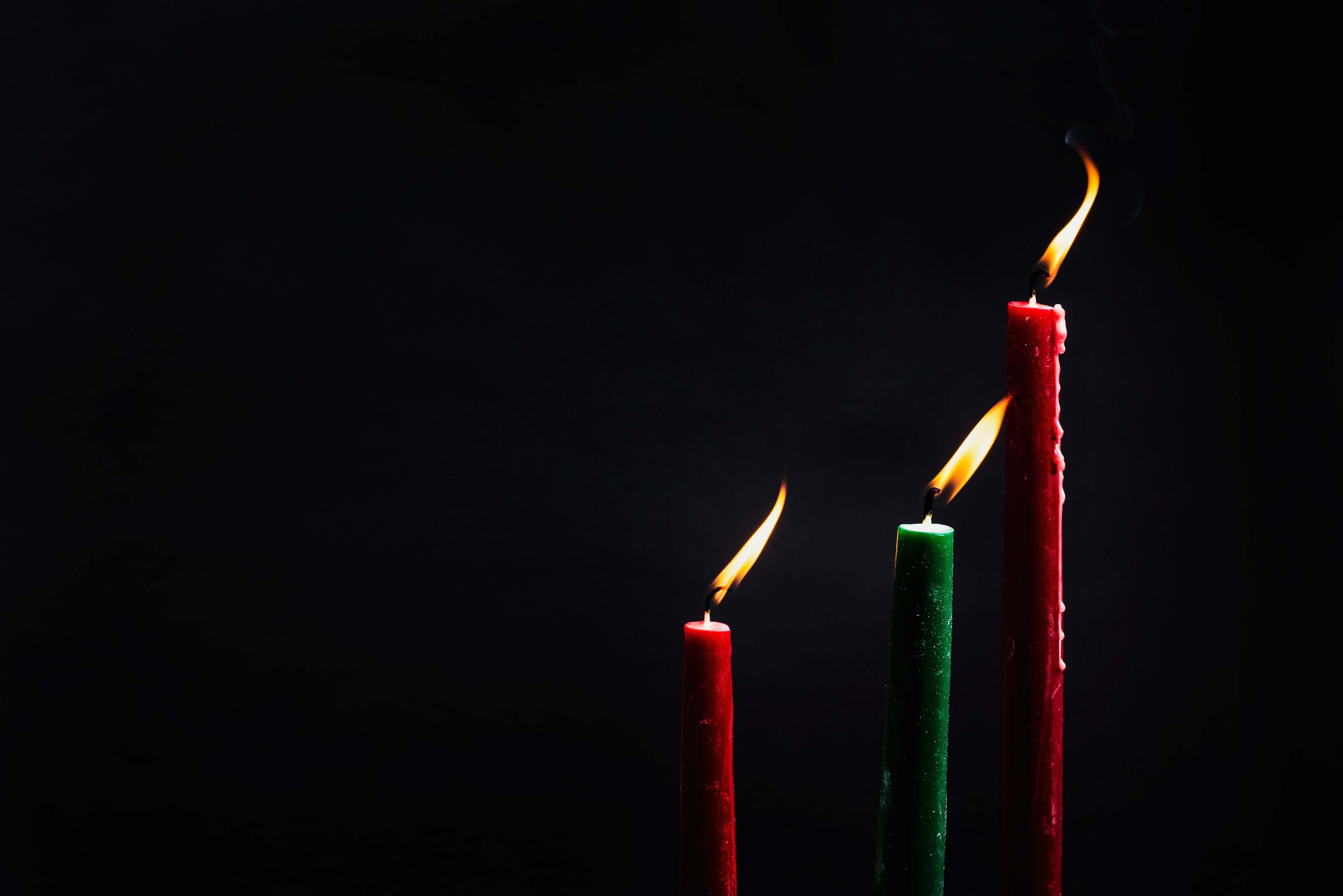 Two red and one green lit Hanukkah candle against a black background.