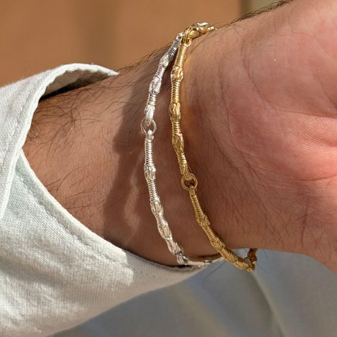 Lifestyle close-up of a wrist wearing the Breindell Tzitzit I Bracelet in 14K Gold and 925 Sterling Silver stacked together. The arm is leaning against a pillar, showcasing the polished architectural links and tonal contrast of the mixed metals. Handcrafted Israeli jewelry featuring symbolic 613 and 39 winding motifs.